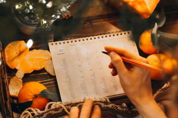Planner page with Christmas sweets, mandarin oranges and candles decoration. new year preparation concept. Planning new year. Female hand hold red pen making notes in January Month dates at night eve