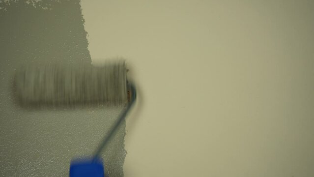 Applying beige paint with a roller brush to the wall. Close up
