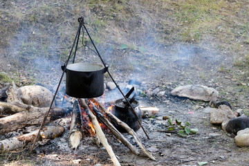 A saucepan on a tripod is hanging on the fire. Cooking while hiking in a tourist camp. Outdoor camping food.