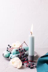 Simple postcard with  blue burning candle, white roses, blue wild berries and teal napkin  on light background. Selective focus. Still life. Romantic postcard. Place for text.
