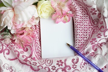 A bouquet of pink flowers and a notepad for notes on a light pink lace background. View from above. Still life in pink tones. Background for a greeting card.