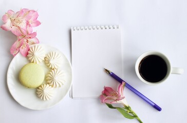 A cup of coffee, macaroons, pink flowers of alstroemeria and a notebook for notes - a festive breakfast of a business person. View from above. Still life in pink tones. Background for a greeting card.