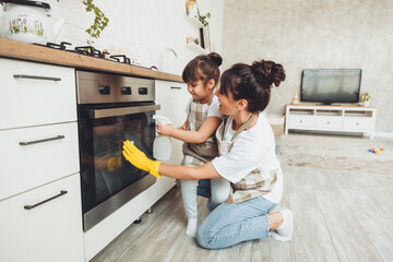 A little girl and her mother are cleaning the kitchen. a woman and a child wipe the oven in the...