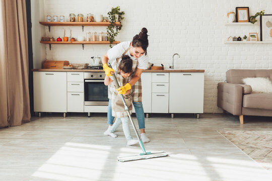 a little daughter and her mom clean the house, a child washes the kitchen floor, a cute little helper girl cleans the floor with a mop, a happy family cleans the room.