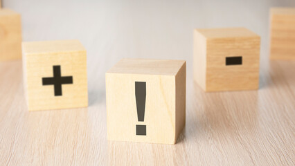 sign exclamation mark, plus, minus sign on the faces of a wooden cube. mini wood cubes on wooden...