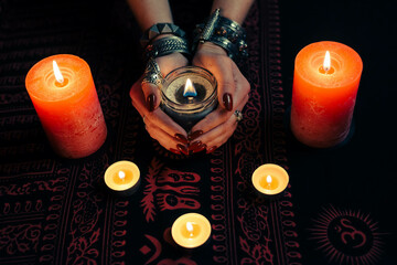 Women's hands  with bracelets and rings holding a burning candle in the dark. 