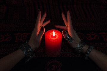 Women's hands  with bracelets and rings holding a burning candle in the dark. 