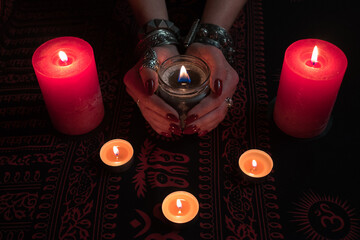 Women's hands  with bracelets and rings holding a burning candle in the dark. 