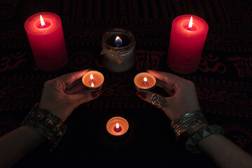 Women's hands  with bracelets and rings holding a burning candle in the dark. 