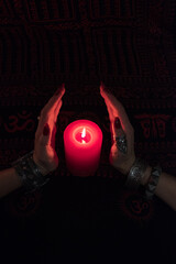 Women's hands  with bracelets and rings holding a burning candle in the dark. 