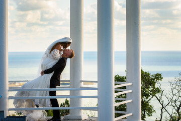 The newlyweds kiss in a beautiful picturesque gazebo against the backdrop of the sea