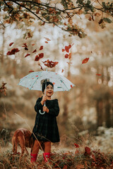 Dziewczynka w lesie trzyma parasol przed opadającymi liśćmi