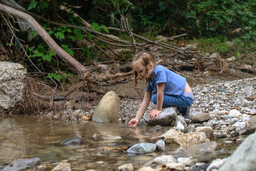Fototapeta na wymiar a little girl during a family hike in the mountains collects water from a mountain river in her palm