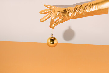 A woman's hand with an elegant golden glove holds a Christmas ball for decoration. Minimal New Year's concept