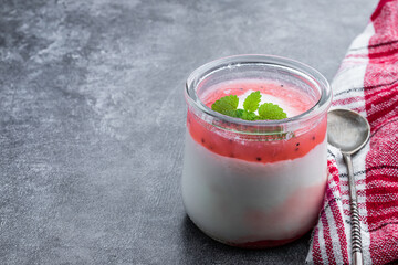Fresh natural homemade organic yogurt with berry jam and chia seed in a glass jar on gray background