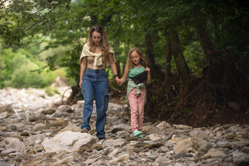 mother with her daughter make a walk near the mountain river on the rocks, family active leisure at the weekend
