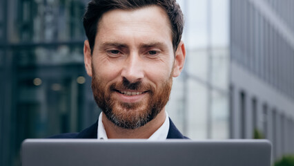 Close-up smiling handsome young man looking at laptop screen happy businessman surfing internet outdoors male journalist writing article agent consultant communicating with client responding to email