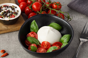 Fresh Italian burrata with tomatoes and basil on plate on grey stone kitchen table, close up. Burrata cheese ball made from mozzarella and cream. Healthy food