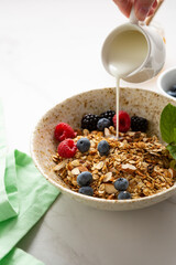  granola with nuts in white bowl breakfast food concept pouring milk