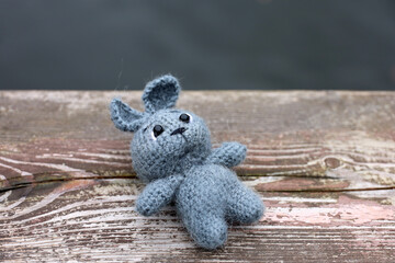 Grey knitted rabbit lying on wooden board on water background. Festive card with toy, knitting concept