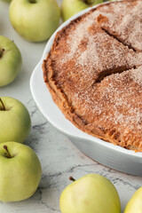 Homemade apple pie on the white marble background with cinnamon flavor covered with sugar Flaky Crust surrounded by green apples.