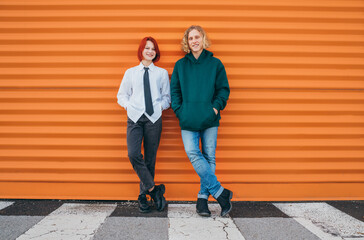 Portraits of two smiling caucasian teen friends boy and girl posing for photo while they standing near the orange wall background. Careless young teenhood . time concept image.