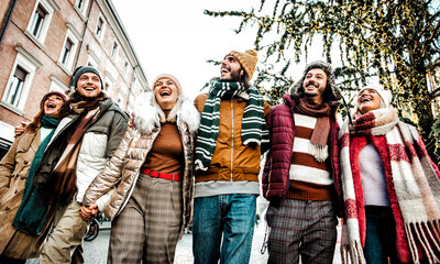 Fototapeta premium Smiling friends walking embraced on the city - Happy group of young people enjoying the day standing outside in winter clothes - Friendship concept with boys and girls laughing during xmas holidays