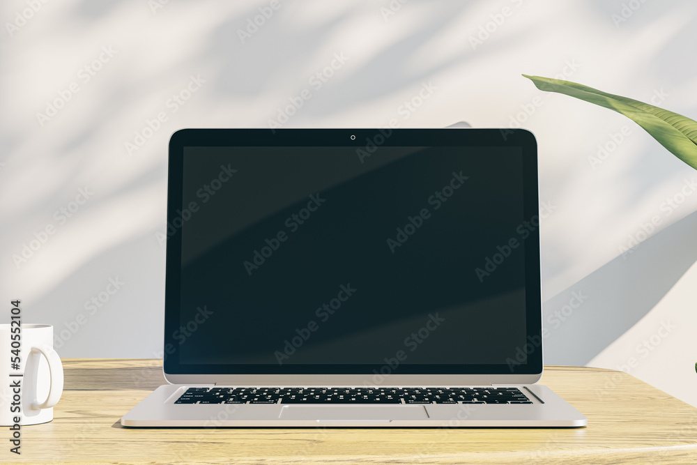 Poster designer office desktop with empty laptop display with mock up place in frame, concrete wall background with sunlight and shadows, blurry decorative plant and coffee cup. 3D Rendering.