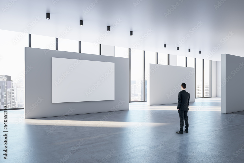 Poster businessman looking at blank white poster with space for your text or logo on light partitions in su
