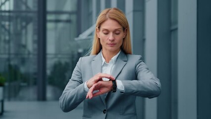 Serious sad businesswoman standing outdoors looking around waiting for business meeting impatient woman dissatisfied looks at wristwatch checks time on watch annoyed by being late lateness concept