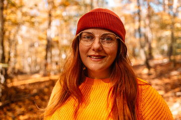 Redhead young woman in a yellow cozy sweater walks in the park. Autumn beauty portrait of a fashionable woman at sunset. Autumn landscape, calmness, tranquility, travel.