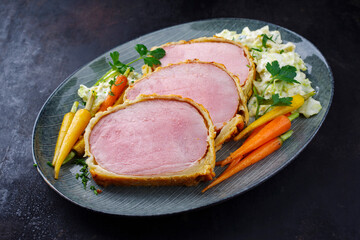 Gebackenes Kasseler Schweinesteak im Teigmantel mit Wirsing Kohl und Baby Karotten serviert als Draufsicht auf einem Design Teller 