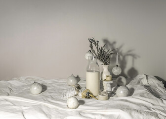still life with a glass carafe of milk, white Christmas tree toys, white candles on a white...