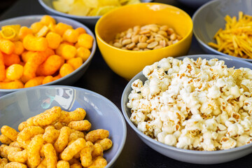Salty snacks assortment shot on dark slate table. The picture includes potato chips, popcorn, peanut, cheese sticks, ketchup sticks, tzatziki chips, smoky flips, and others