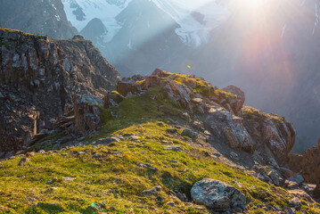 Obraz premium Sunny mountain view from cliff at very high altitude. Scenic alpine landscape with beautiful sharp rocks and couloirs in sunlight. Beautiful scenery on abyss edge with sharp stones and green grass.