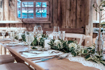 Wooden  table are glasses, candles. Table is decorated with compositions of eucalyptus branches and sprig of Italian greenery