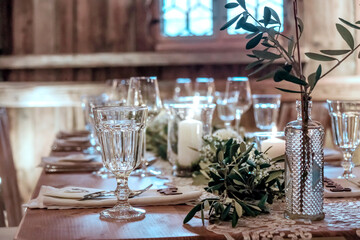 Wooden  table are glasses, candles. Table is decorated with compositions of eucalyptus branches and sprig of Italian greenery