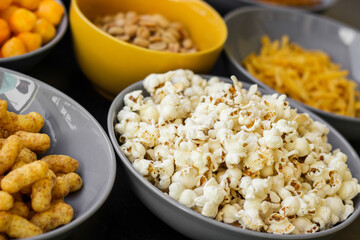 Salty snacks assortment shot on dark slate table. The picture includes potato chips, popcorn, peanut, cheese sticks, ketchup sticks, tzatziki chips, smoky flips, and others