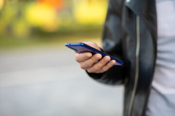 Closeup shot of an young modern man holding mobile phone in hand, blurred background