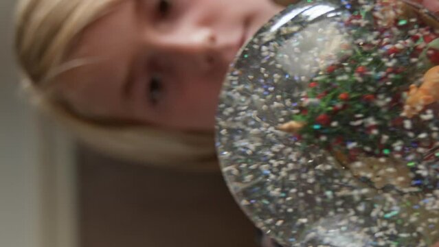 Cute caucasian boy shaking Christmas snow globe at home. Focus on snowglobe