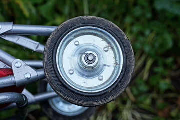 small dirty gray black metal and plastic wheel on a trolley outdoors on a green background - Powered by Adobe