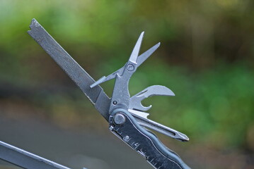 part of gray metal multitool on a green background - obrazy, fototapety, plakaty