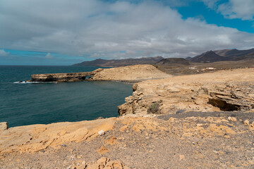 Fototapeta na wymiar Beach with dark sand, waves of Atlantic Ocean and harsh volcanic mountains in the background. La pared - Fuerteventura (canaries islands)
