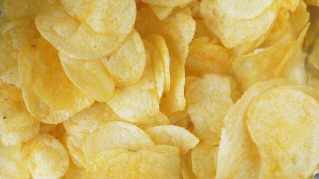 A woman's hand takes one crispy snack. A pile of unhealthy food lies on the table. People take chips, the video is shot close-up.