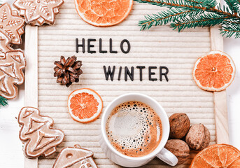 Lettering hello winter on letter board. Fir branches, dried oranges, nuts and a cup of coffee. minimalistic new year background 2023