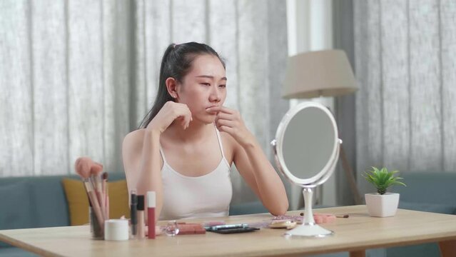 Worried Young Asian Woman Looks In The Mirror And Popping Pimples While Applying Makeup At Home
