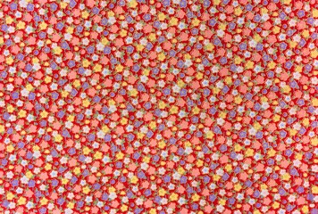 Close up on a high detailed photograph of a Japanese furoshiki cloth made in cotton fabric with a pattern design illustrated with colorful flowers enhanced with golden threads on a red background.