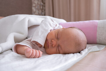 Fototapeta na wymiar cute little newborn baby girl peacefully sleeps in the nursery on a white cotton bed