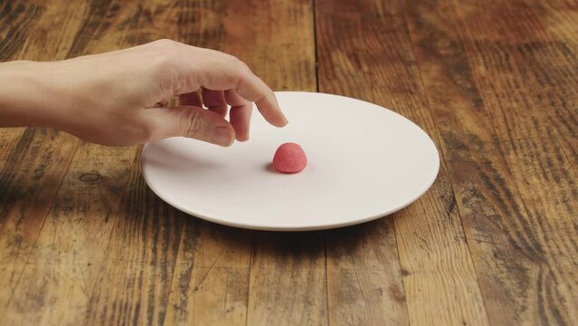 Une main de femme prend le dernier bonbon fraise en h&eacute;sitant dans une assiette blanche