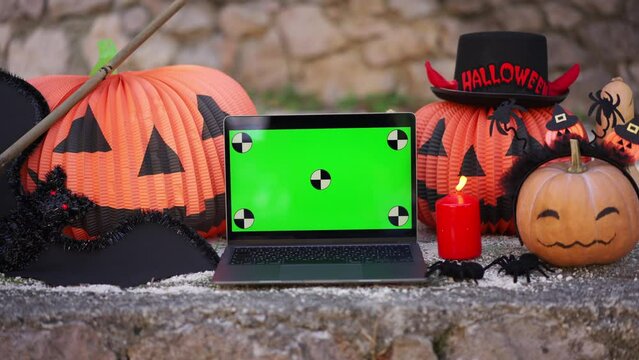 A laptop with a green screen with dots for tracking movement against the background of Halloween props, bats, pumpkins, skulls, spiders, brooms, burning candles. The concept of application advertising